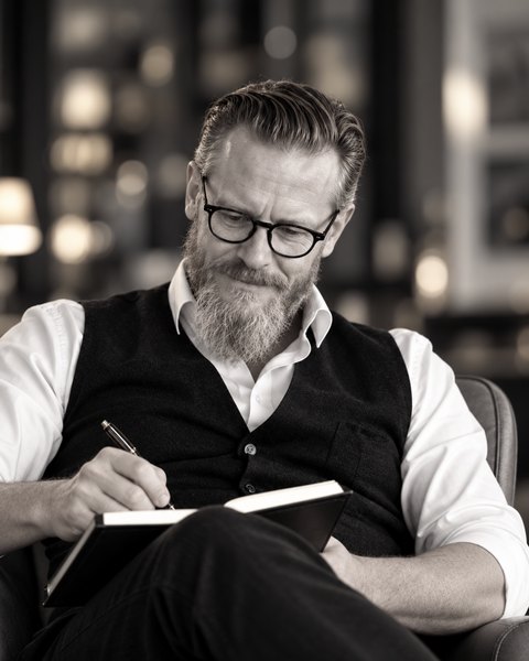 Mirko Schwerdtfeger in Hemd und Weste, schreibt mit einem Füller in ein Notizbuch